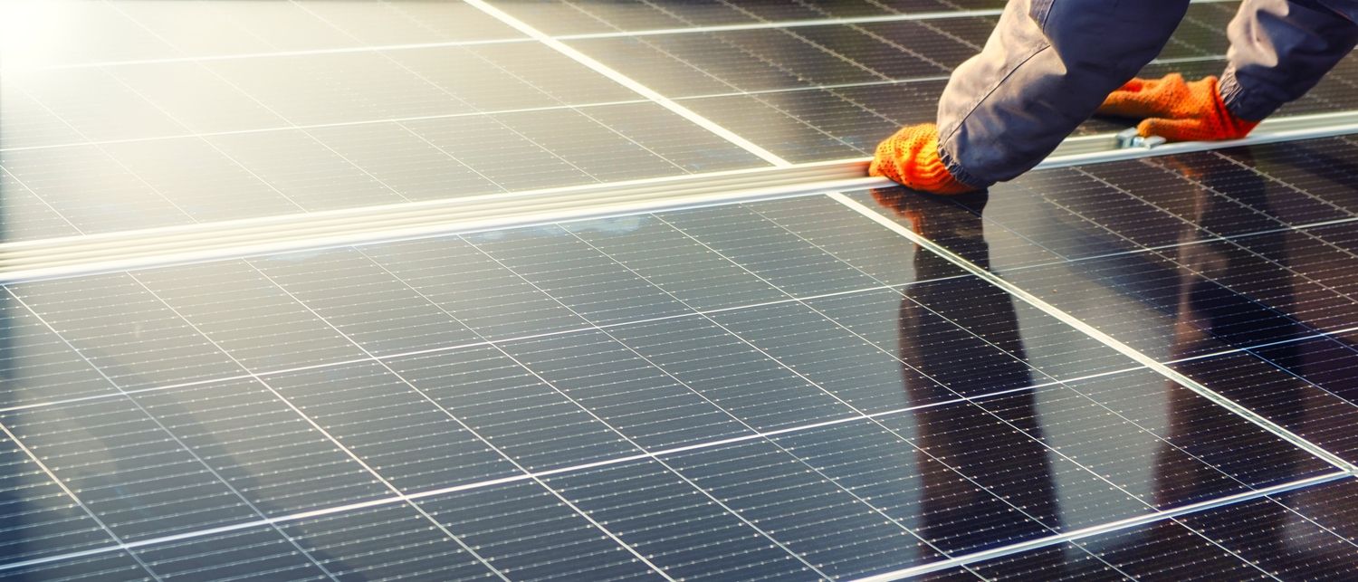 Eine Person mit orangenen Arbeitshandschuhen verlegt Photovoltaik-Anlagen
